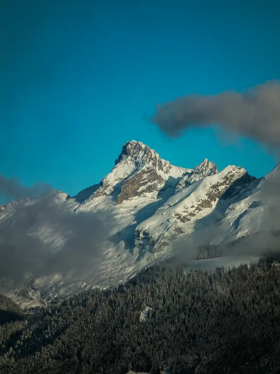 Sommet enneigé entre les nuages et le ciel bleu.